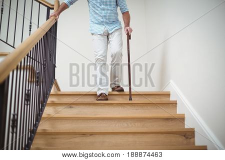 Senior man climbing downstairs with walking stick at home