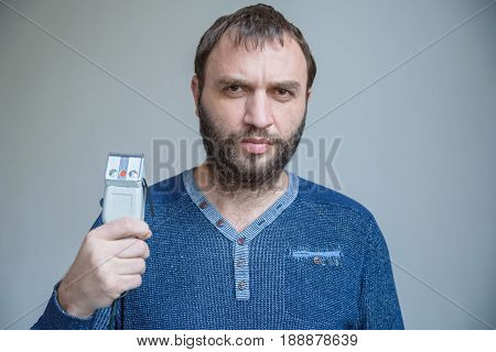 Handsom bearded man in blue sweater holds electric shaver