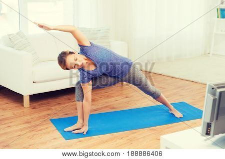 fitness, sport, people and healthy lifestyle concept - woman making yoga bikram triangle pose on mat and watching tv lesson