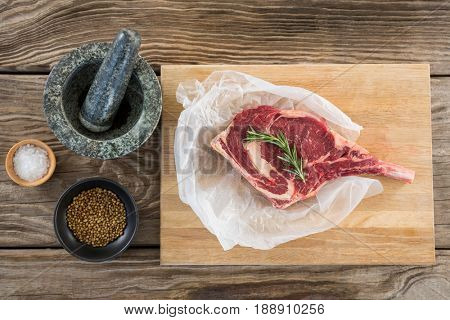 Raw Rib chop, rosemary herb, salt, corainder seeds and stone grinder against wooden background