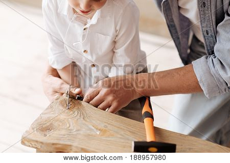 Being in workshop. Handsome boy bowing head while looking downwards and keeping pliers in both hands