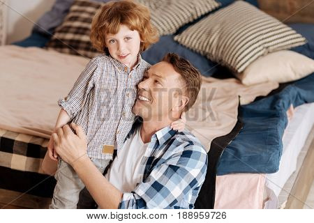 Love my daddy. Attractive boy with curly hair looking straight at camera and keeping left hand on the neck of his father