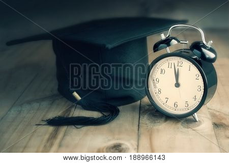 graduation cap with alarm clock on wood board .