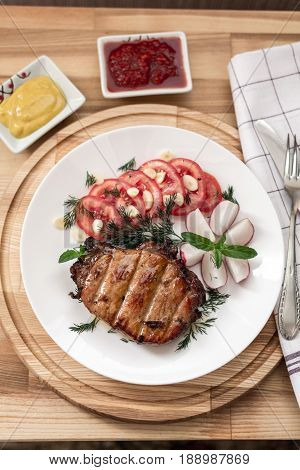 Pork Steak Cooked On The Grill Is Decorated With A Tomato, Radish, Dill, Parsley, Garlic Greens, Min