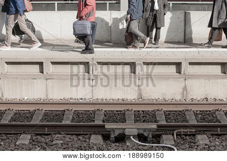 Travelers moving on railway station platform to catch train to arrive on railroad tracks at bottom of concrete platform