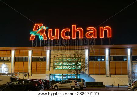 Roncq,france-february 27,2019: Night View Of Auchan Supermarket Logo, Entrance And Parking.auchan Is