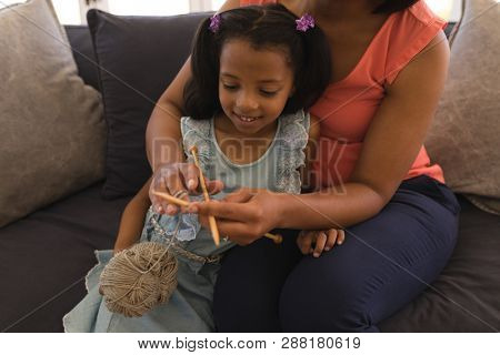 Close-up of an African American grandmother teaching her granddaughter how to knitt in living room at home