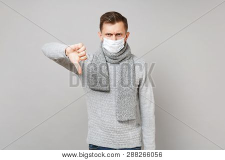 Dissatisfied Young Man In Gray Sweater, Scarf Sterile Face Mask Showing Thumb Down Isolated On Grey 