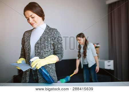 Beautiful Brunette Caucasian Mother And Daughter Cleaning Together In Room. Young Woman Spray On Spo