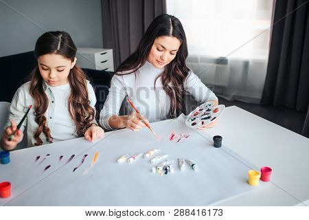 Beautiful Brunette Caucasian Mother And Daughter Paint Together In Room. They Sit At Table And Draw.