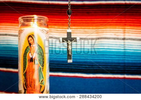 Wood And Silver Crucifix With Virgin Mary Prayer Candle To The Left, With Mexican Blanket As Backdro