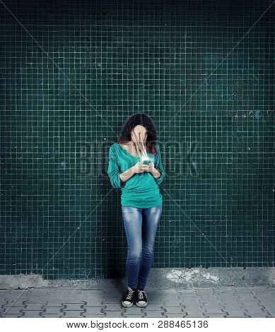 Woman Using Smartphone Against A Wall. The Concept Of Phone Addiction. Face Absorbed By The Phone.