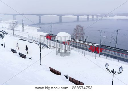 Winter Snowy Landscape With Electric Multiple Unit Train Moving Along The River Bank With A Vintage 