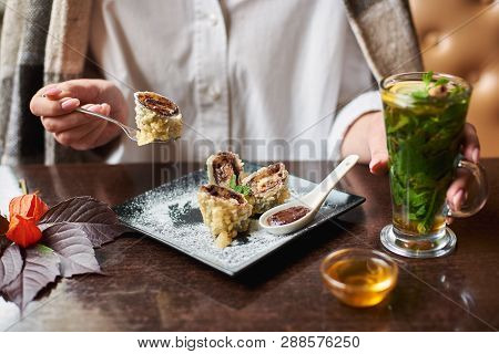 Crop Of Girl In White Holding Drink In Hand And Eating Tasty Sweet Sushi Roll With Chocolate Sauce. 