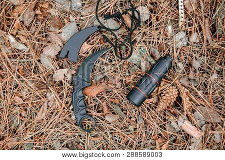 Monocle And Karambit Knife On The Ground Covered With Pine Needles