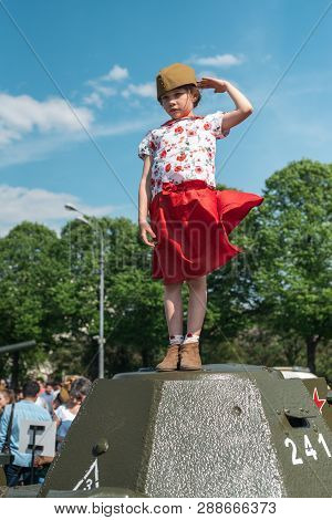 Moscow, Russia - May 9, 2016. Little Girl In A Red Skirt And Forage-cap Is Standing On A Tank Of The