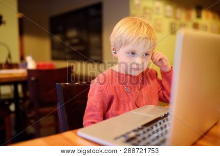 Cute Little Boy Watching Cartoon Movie Using Computer In The Cafe Or Restaurant. Child Communication