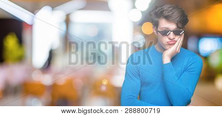 Young man wearing funny thug life glasses over isolated background thinking looking tired and bored with depression problems with crossed arms.