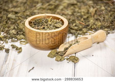 Lot Of Pieces Of Dry Green Tea In A Scoop With Wooden Bowl On White Wood