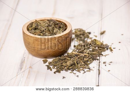 Lot Of Pieces Of Dry Green Tea With Wooden Bowl On White Wood
