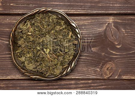 Lot Of Pieces Of Dry Green Tea With Copyspace In Old Iron Bowl Flatlay On Brown Wood