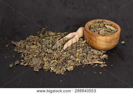 Lot Of Pieces Of Dry Green Tea With Wooden Bowl On Grey Stone