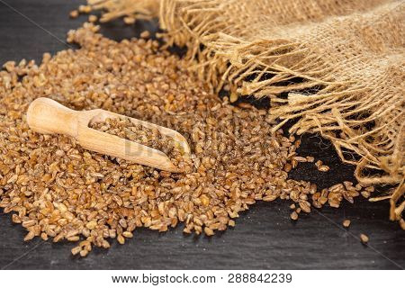 Lot Of Whole Raw Bulgur Grains Jute Cloth With Wooden Scoop On Grey Stone