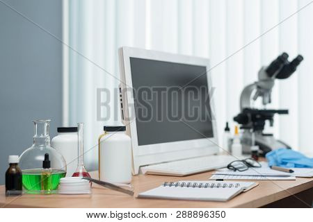 Laboratory Table With Microscope, Flasks And A Desktop Computer Above On A Window Light Background. 