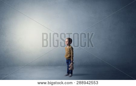 Little waggish kid staying alone in a big empty room with his plush