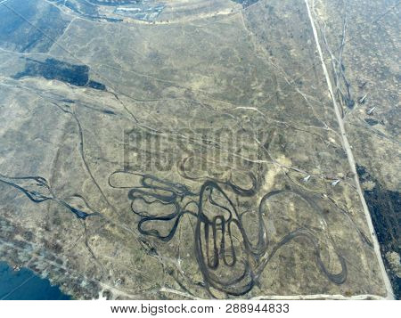 Curved pattern of dirt road, similar to the lines drawing geoglyphs of the Nazca desert.Aerial view of the countryside (drone image).Near river Desna.Winter time.Sunset. March8, 2019.Near Kiev,Ukraine