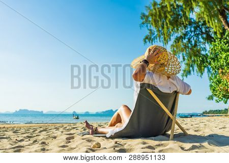 Woman with straw hat enjoying her holidays on a transat at the tropical beach in Thailand