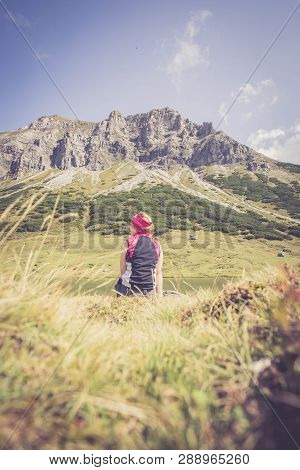 Mountain Climber Is Sitting On The Ground And Doing A Break During A Hike. Enjoying The View Over Th