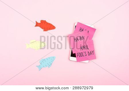 April Fools' Day Celebration Background With Paper Fish, Smartphone And Sticky Note On Pink Backgrou
