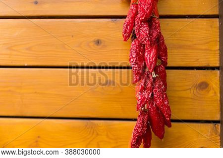 Red Chili Peppers On The Background Of The Old Wooden Wall.string Of Fresh Organic Peppers Is Hangin