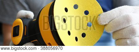 Close-up Of Professional Craftsman Changing Disc On Electrical Yellow Sander. Worker Wearing Protect