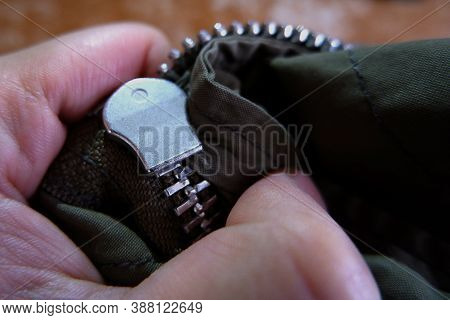 A Close Up Of Stuck Zipper On A Dark Green Jacket, Holding By A Hand