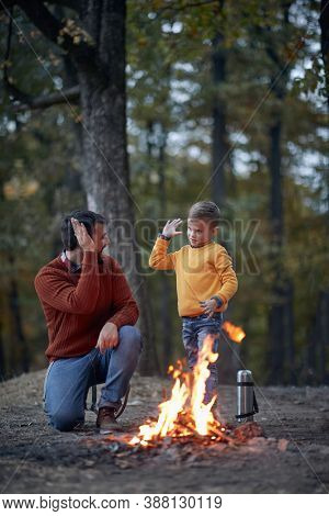 Father and son starting a fire together on a camping; Spring or autumn camping with campfire at night ; camping, travel, tourism, hike and people concept. Quality family time together.