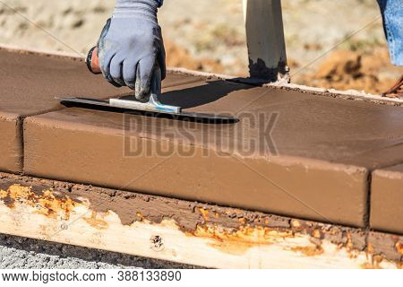 Construction Worker Using Trowel On Wet Cement Forming Coping Around New Pool.
