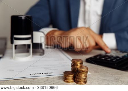 Man Is Counting Profit On A Calculator, Stack Of Coins On Desk In Office. Economy And Management Fin