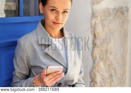 Portrait Of Beautiful Young Caucasian Business Woman With Smartphone Wearing Siut At The Door On The