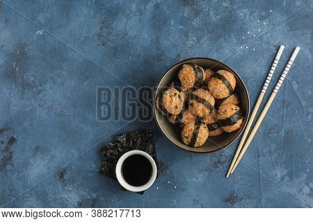 A Bowl Of Rice Balls With Sesame Seeds And Nori Seaweed, Served With Soy Sauce, Chopsticks On A Dark