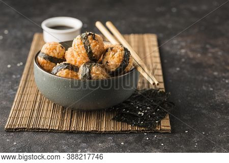 A Bowl Of Rice Balls With Sesame Seeds And Nori Seaweed, Served With Soy Sauce, Chopsticks On A Dark