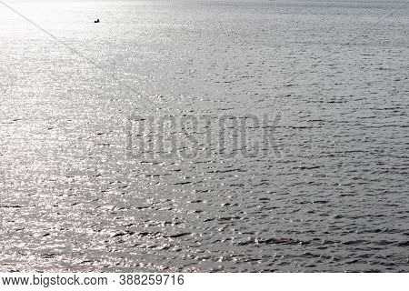 Early In The Morning Water Ripples On A Surface Lake In The Distance A Small Boat With Fishingman