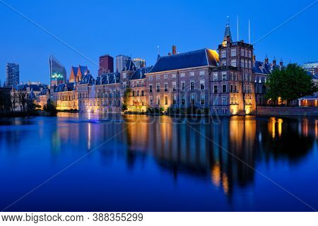 View of the Binnenhof House of Parliament and the Hofvijver lake with downtown skyscrapers in background illuminated in the evening. The Hague, Netherlands