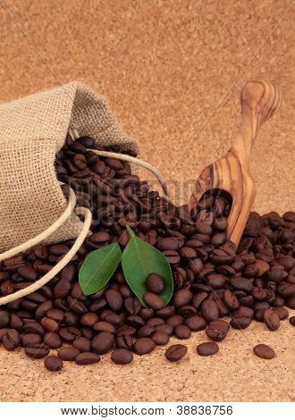 Koffie bonen in een koord van de Hessiaan ontslaan en los met blad takjes op cork achtergrond.