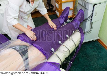 The Beautician Of The Spa Salon Covers The Legs Of A Woman In A Special Suit For Pressotherapy.
