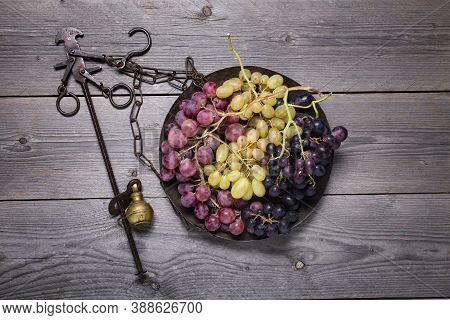 On A Rustic Wooden Surface, An Old Steelyard, With Various Types Of Table Grapes