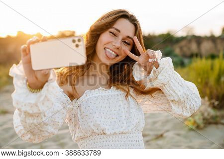Young caucasian attractive brunette woman smiling and taking selfie phoro on cellphone outdoors