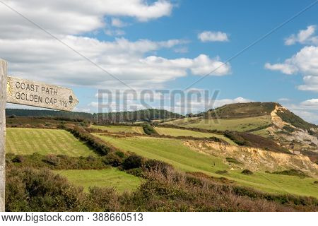 Close Up Of A Wooden Signpost Pointing To Golden Cap Mountain With Golden Cap Mountain In The Backgr