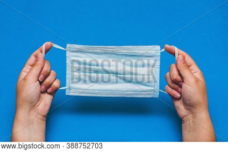 Person Hands Holds Blue Medical Disposable Mask Made Of Cotton. First Person View, Blue Background.